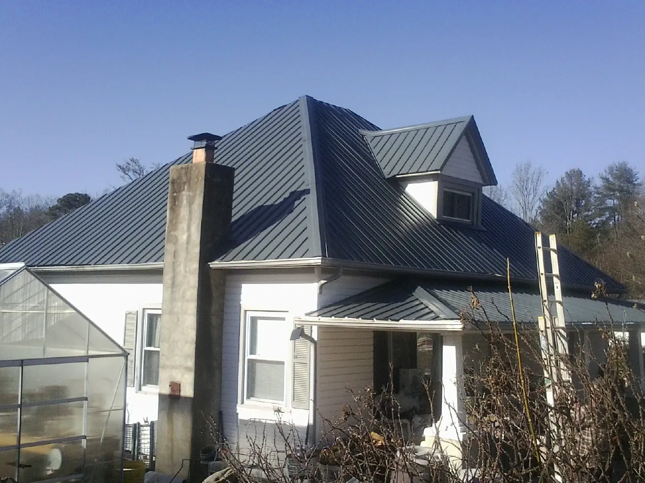 Dark blue standing seam metal roof on a white farmhouse with dormer — Slate & Tile Roof Repair by Roofing Brothers in Novi
