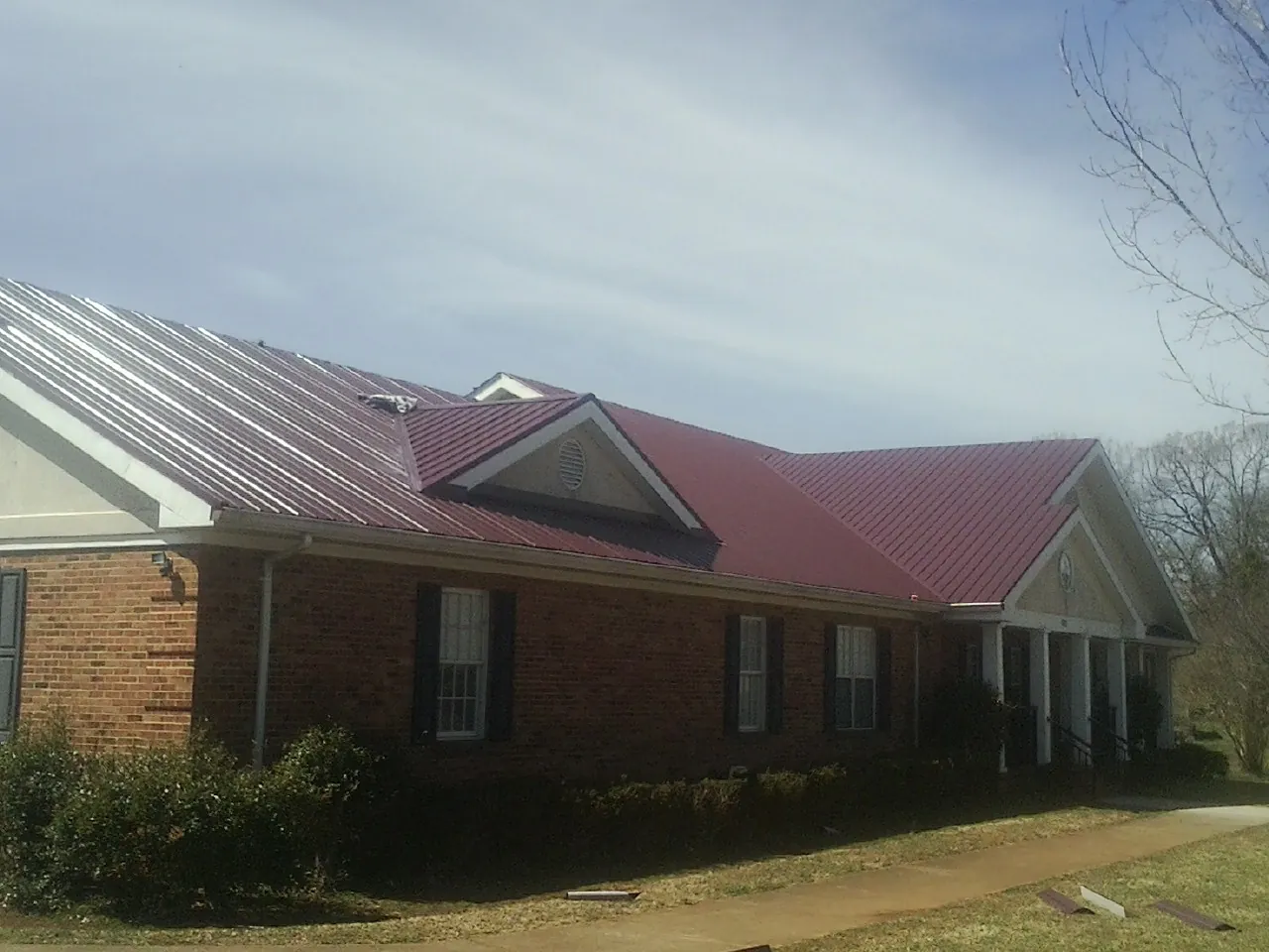 Red metal roof with gabled entries on a long brick building, from a Hail Damage Roof Repair job in Novi