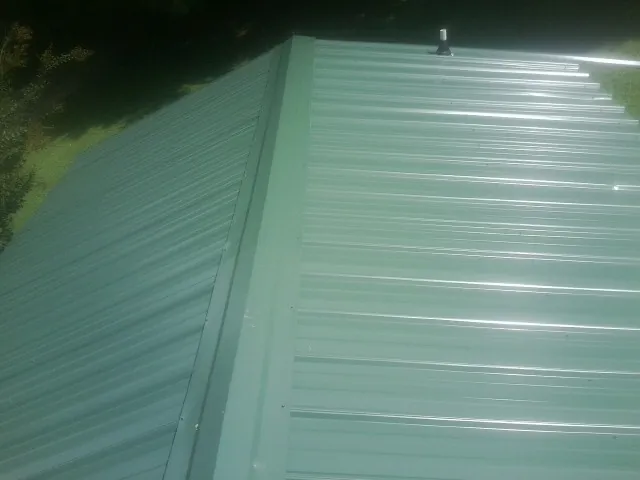 New green metal panels meeting at the ridge of a roof — Flat Roof Repair work by our crew in Novi