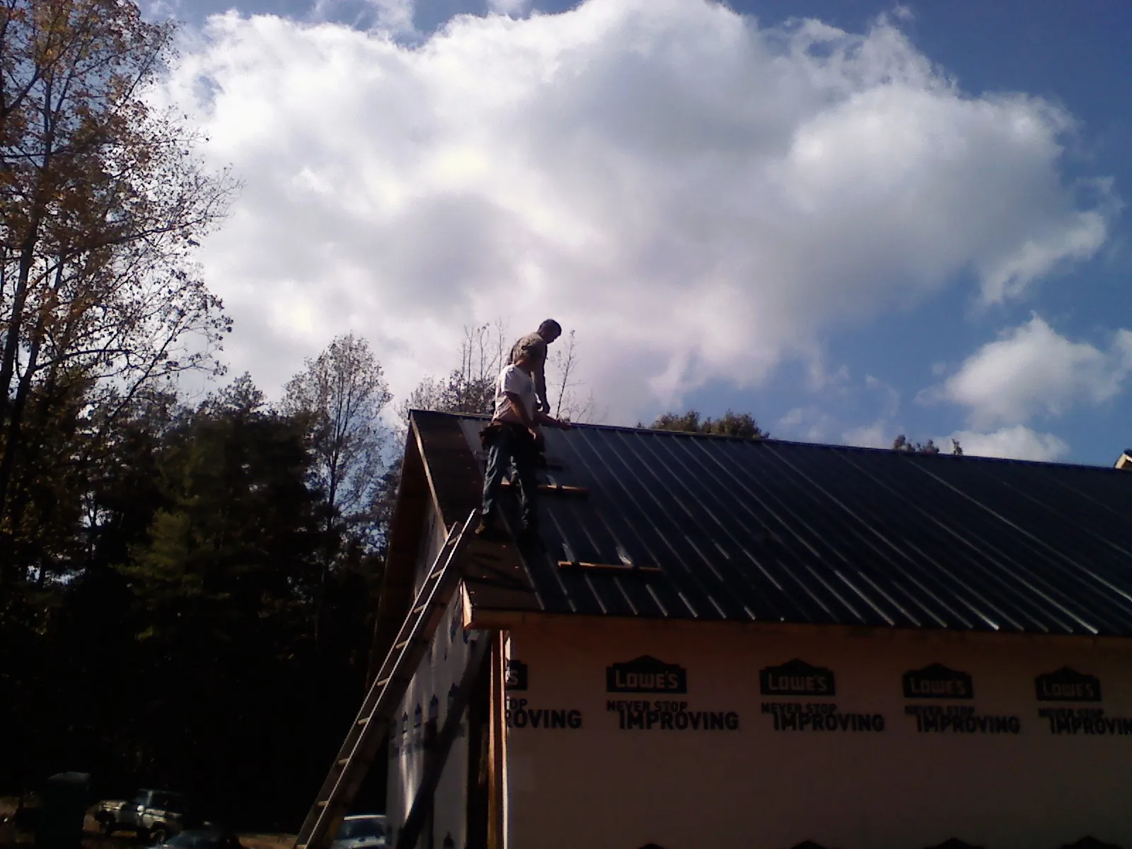 Roofer fastening dark metal panels high against a cloudy sky, from a Roof Inspection job in Novi