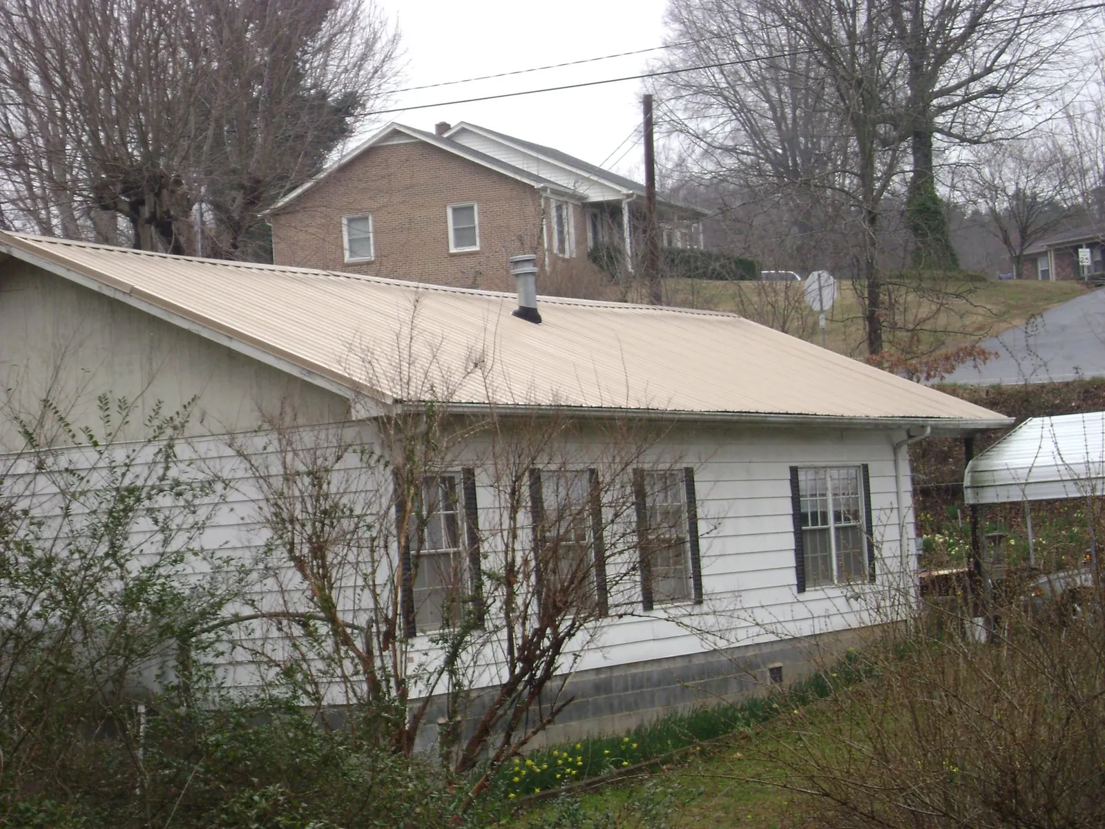 Tan metal roof on a white sided house set into a hillside — Commercial Roofing by Roofing Brothers in Novi